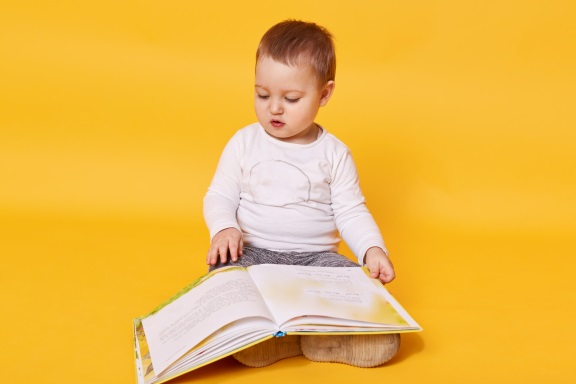 toddler girl pretends read book while sitting floor viewing pictures turning pages little girl looks concentrated